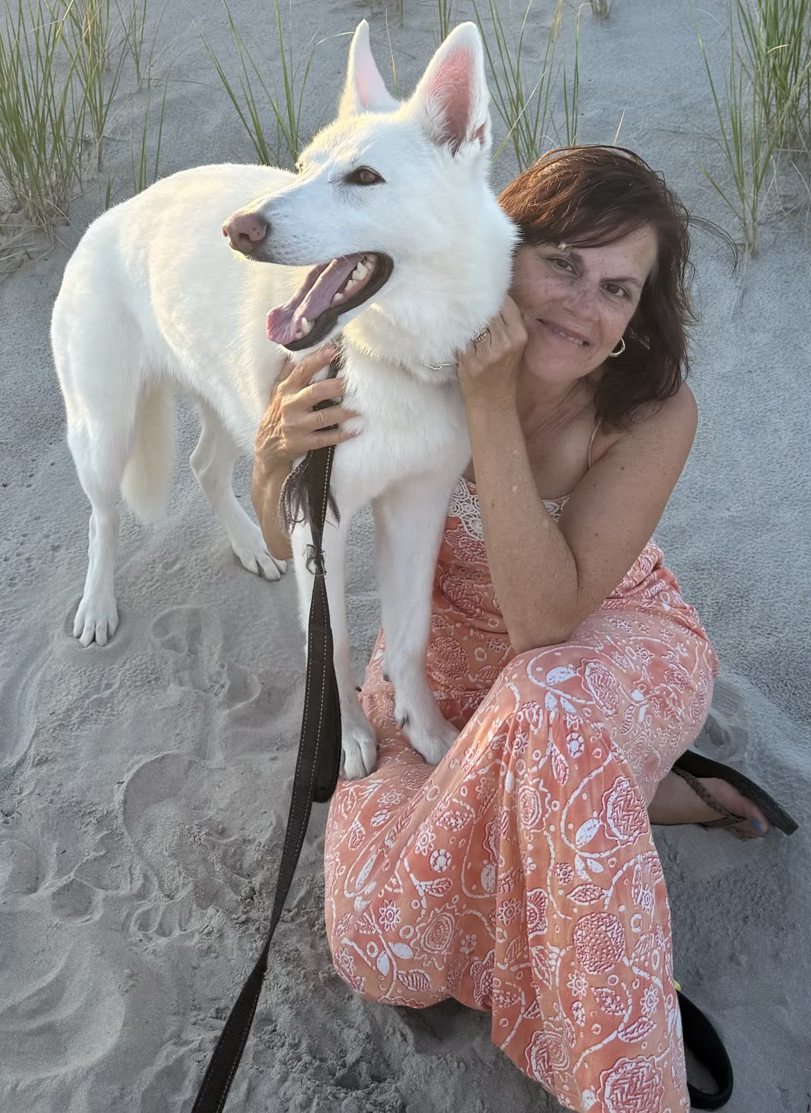 Margaret kneeling in the sand dunes at golden hour with her arm around Ella, who is leaning into her